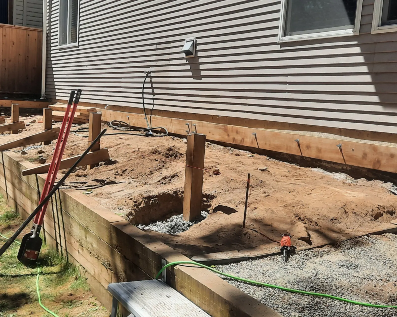 Deck being built beside a house in Chilliwack, with posts set in open dirt and a timber planter wall along the front