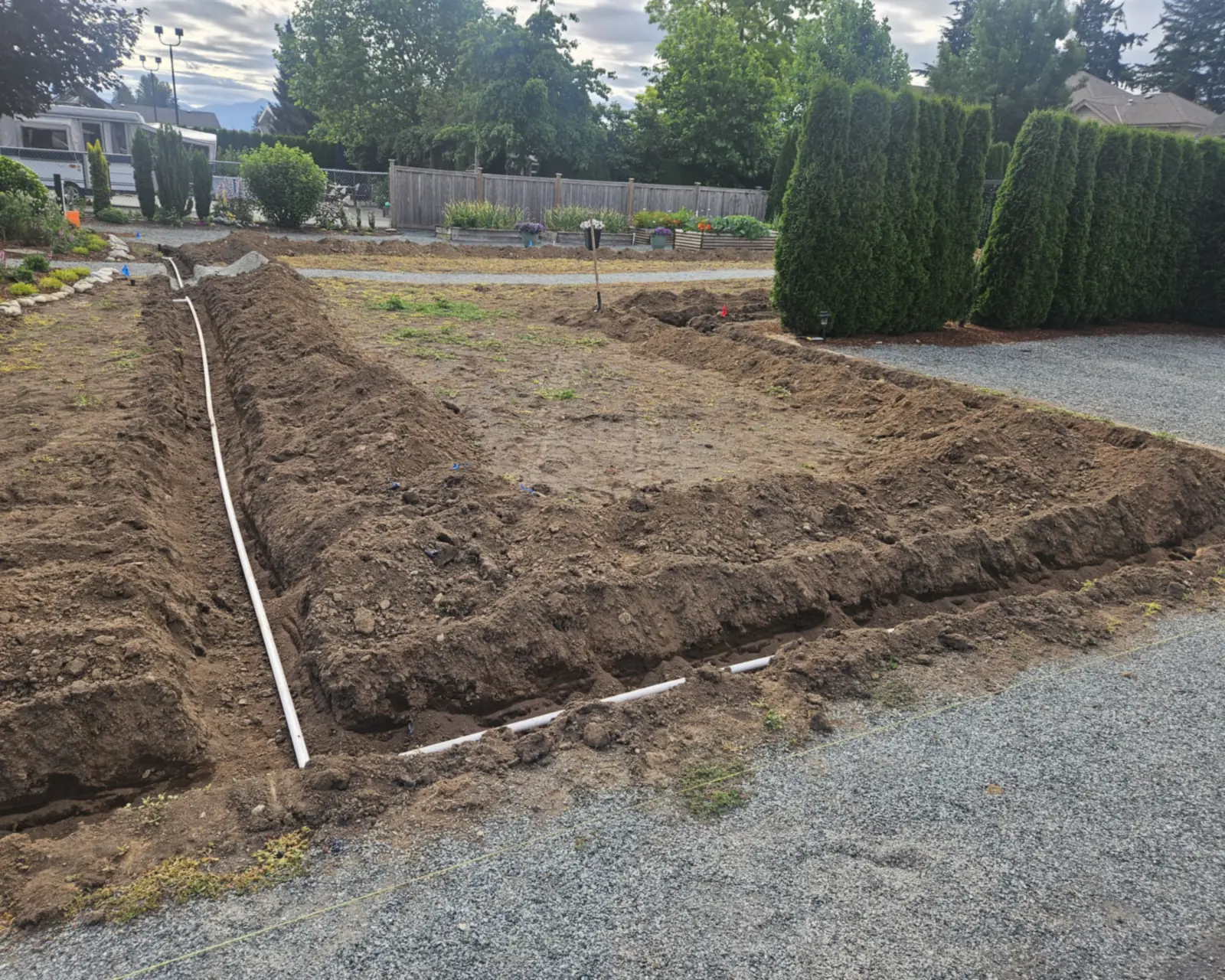 Trenches dug around a yard with white irrigation pipe laid in them before backfill