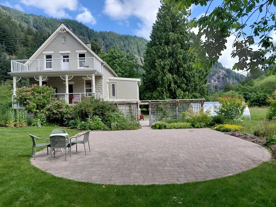 After: round paver patio with table and chairs in the lawn, garden beds and lattice privacy screen, Earthwise Farm, Hope, BC
