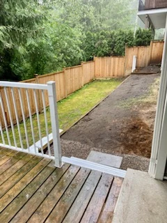 Bare, raked soil strip along the side of a house in Chilliwack, next to a lawn and a cedar fence, seen from the back steps