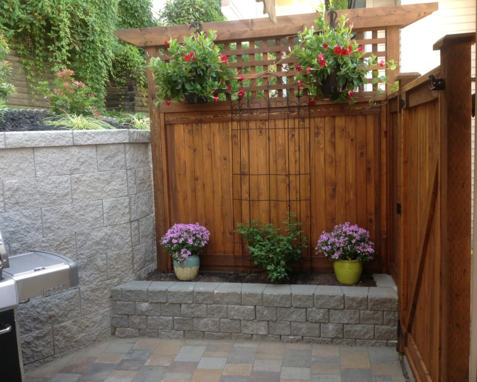 Stained cedar fence and matching gate with a lattice top and hanging baskets, above a block planter on a paver patio